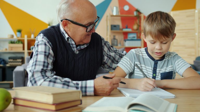 Adult supporting a child who is writing at a table