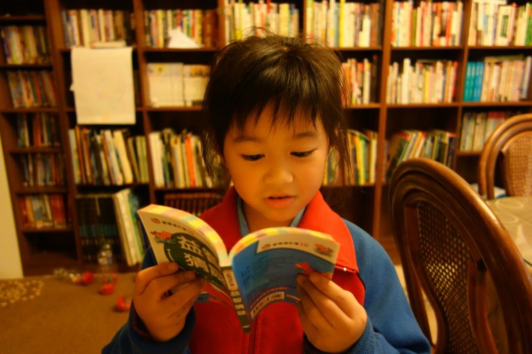 Young child reading a book in front of library shelves